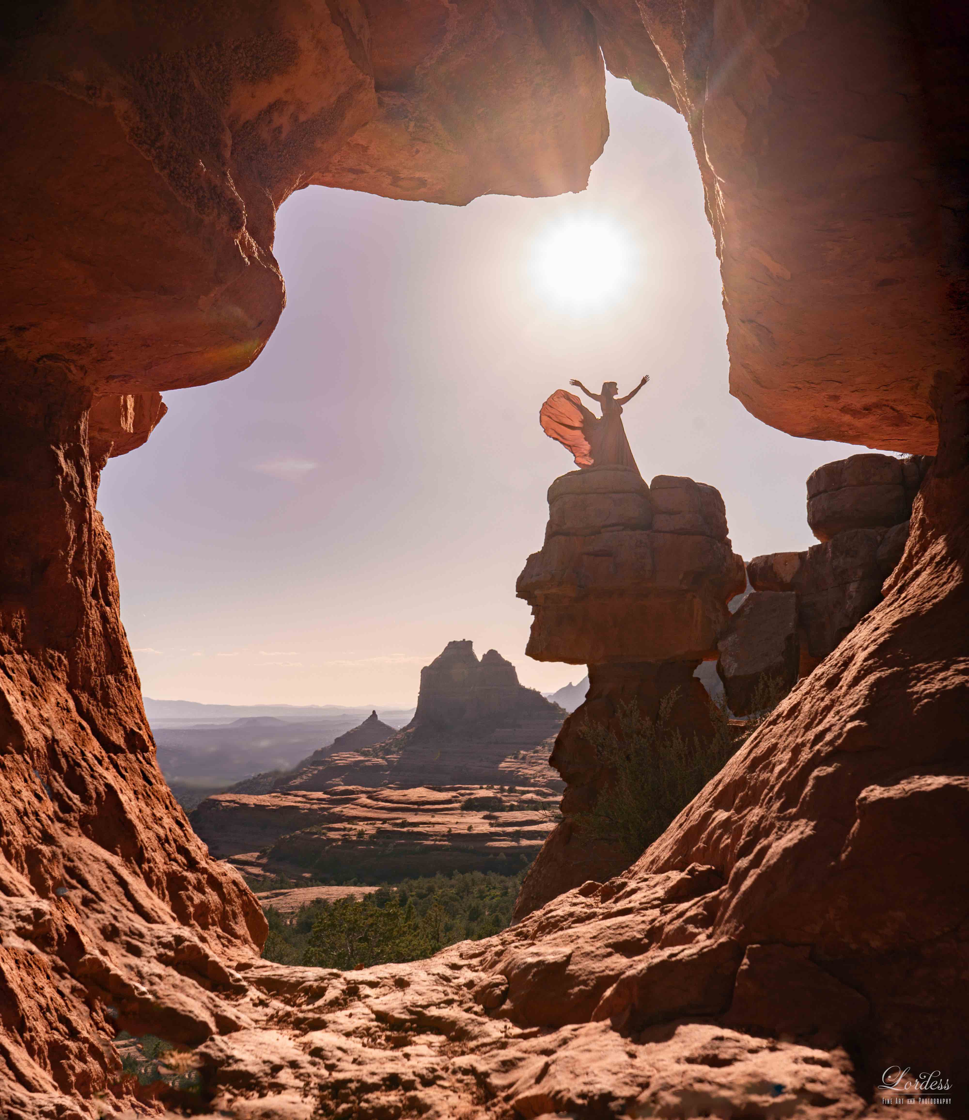 Terii standing on a cliff platform in Sedona, arms raised, framed by a natural rock keyhole, sunlight overhead