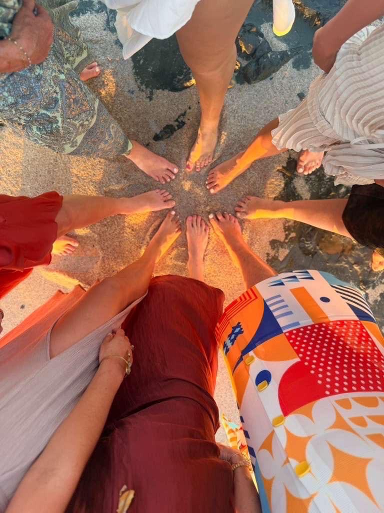 Overhead view of bare feet gathered in a circle on the sand at sunset