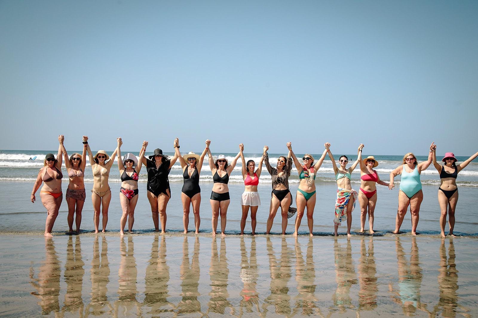 A line of women on the beach holding hands raised to the sky